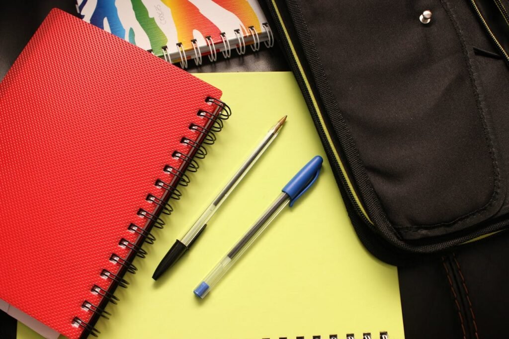 Black and Blue Pens Beside Red Covered Notebook